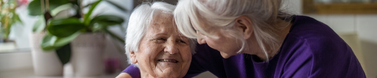 Mujer de unos 60 años abrazando a su madre de 90, la cual sufre de alzheimer, las dos son rubias y a pesar de la enfermedad están muy contentas de estar juntas.