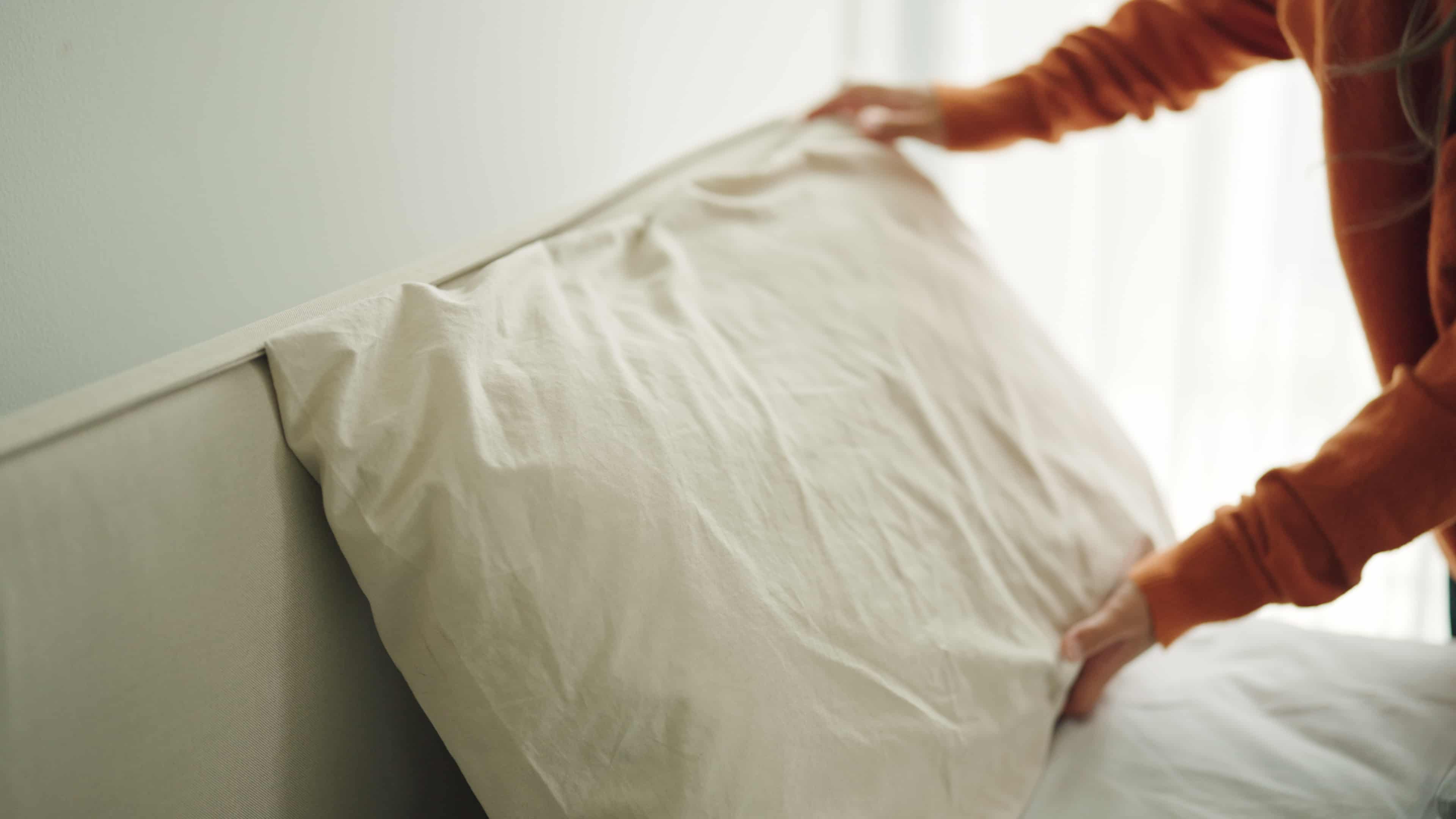 Mujer arreglando el cojín de una cama, de forma sencilla ya que no hay un paciente encamado, cambiar las sábanas con un paciente encamado es una tarea mucho más ardua.
