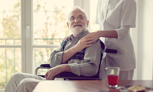 Hombre mayor con esclerosis múltiple recibe ayuda de su cuidadora