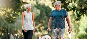 Una mujer y un hombre mayor, sacando a pasear a su perro con ropa deportiva y pasándolo muy bien. Se miran y sonríen. El ejercicio es esencial como estrategia para bajar el colesterol de forma natural.