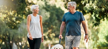 Una mujer y un hombre mayor, sacando a pasear a su perro con ropa deportiva y pasándolo muy bien. Se miran y sonríen. El ejercicio es esencial como estrategia para bajar el colesterol de forma natural.