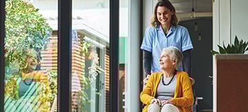 Mujer con demencia y en silla de ruedas, siendo transportada por una enfermera de la residencia. Está ingresada en la residencia ya que llegó el momento en el que no podía vivir más en su hogar.