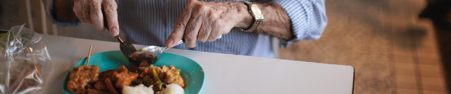 Hombre mayor comiendo un plato de comida, acción que puede ser complicada si sufres de disfalgia, ya que dificulta la ingesta de ingredientes.