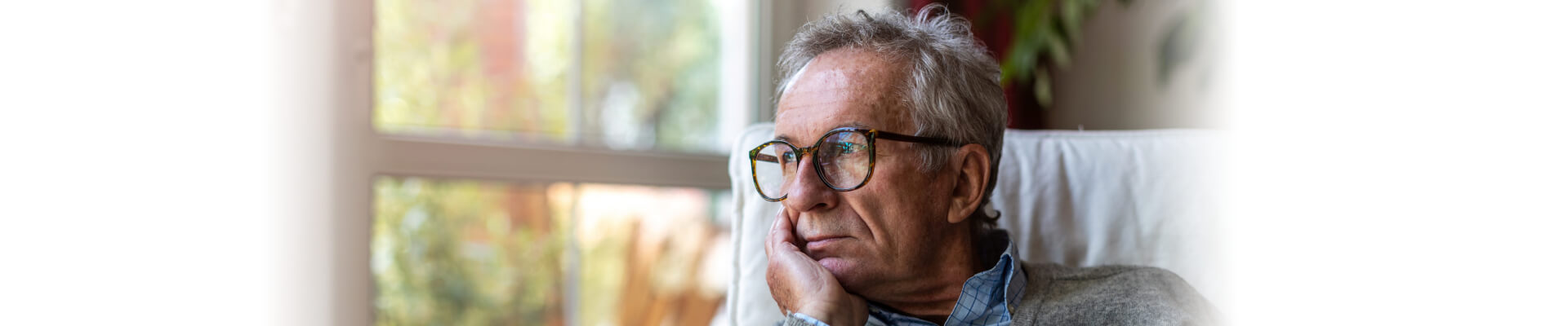 Hombre sentado en el sillón de su casa mirando con cara de preocupación la ventana y apoyando su cabeza en su mano. Está preocupado por el hecho que sufre incontinencia urinaria en hombres. Esto le supone un conjunto de problemas en el dia a dia, pero aún así puede encontrar alguna solución como los ejercicios pensados para solucionar su problema.