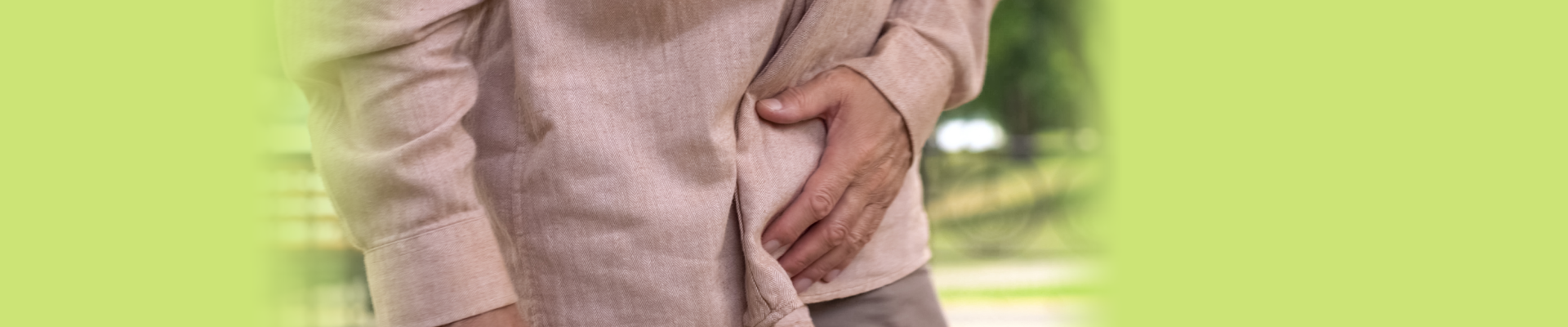 Primer plano de un hombre mayor con camisa rosa en un parque, tocandose la ingle, ya que tiene dermatitis de ingle causada por la incontinencia urinaria.