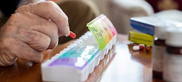 Mano de mujer mayor colocando un medicamento que es bueno para la incontinencia urinaria, en su pastillero. Es decir un objeto para organizador de pastillas según dia de la semana.