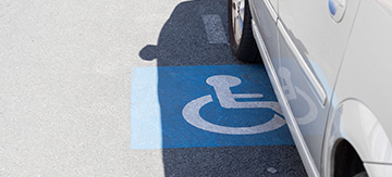 Coche aparcado sobre una plaza de minusválidos, lo sabemos por el simbolo característico sobre el asfalto, indicado entre otros sitios en la normativa de plazas de aparcamiento para minusválidos.