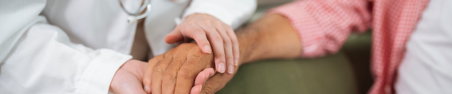 Medico hablando cariñosamente con su paciente que sufre de parkinson. En el momento de la foto, agarra con sus dos manos a la mano de la paciente anciana.