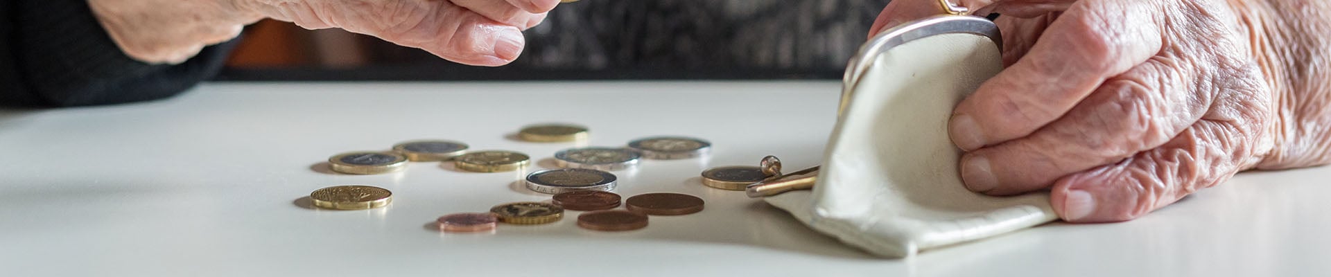 Mujer mayor con un monedero abierto y con unas monedas esparcidas por la mesa. Las está contando, para saber cuánto le queda de su pensión mínima de jubilación.