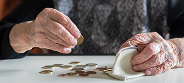 Mujer mayor con un monedero abierto y con unas monedas esparcidas por la mesa. Las está contando, para saber cuánto le queda de su pensión mínima de jubilación.