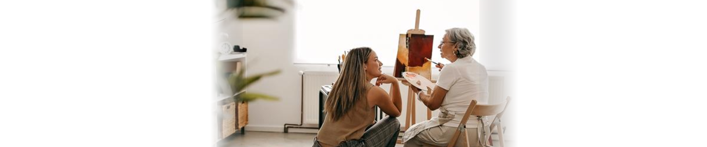 Chica joven acompañando a una mujer mayor en su pasatiempo. Pintar un lienzo blanco y hacer volar la imaginación, las dos lo pasan muy bien pintando.